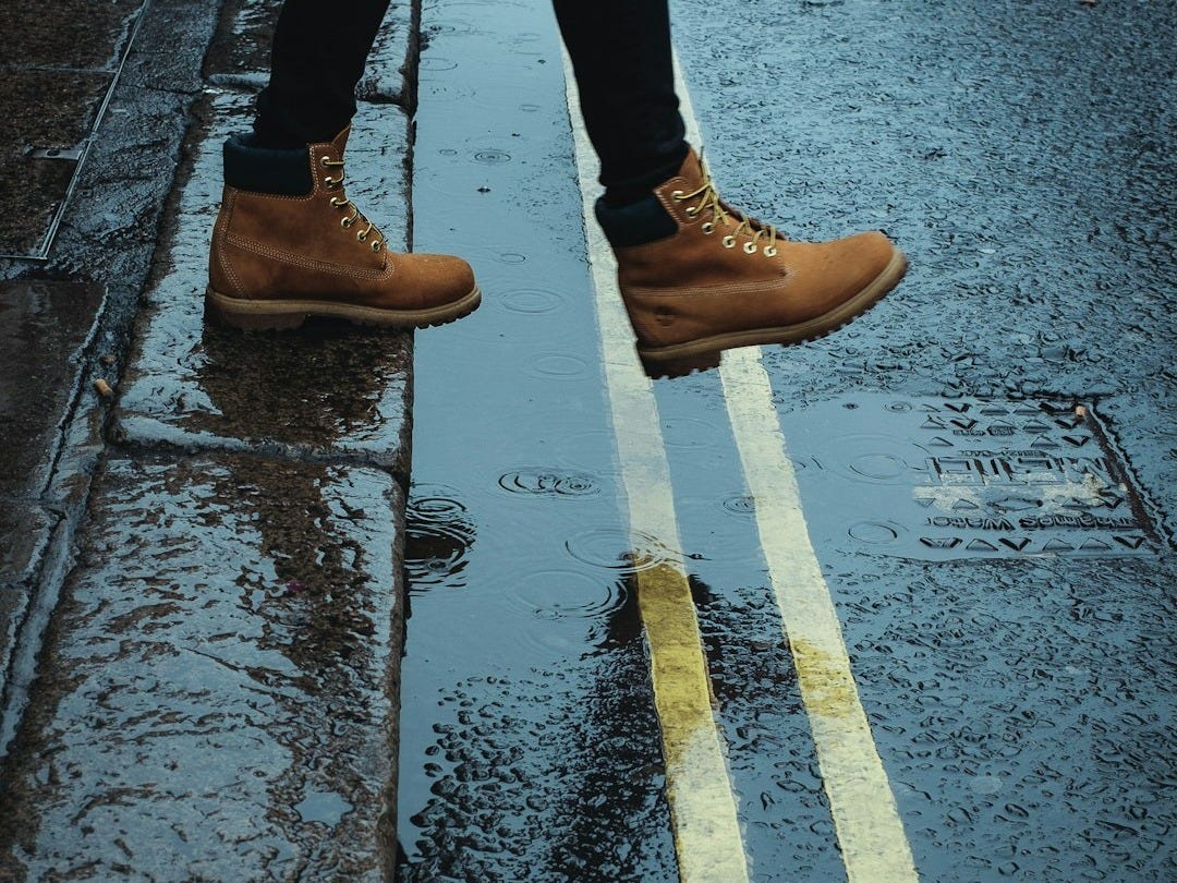 person wearing brown boots walking on a wet road person wearing brown boots walking on a wet road