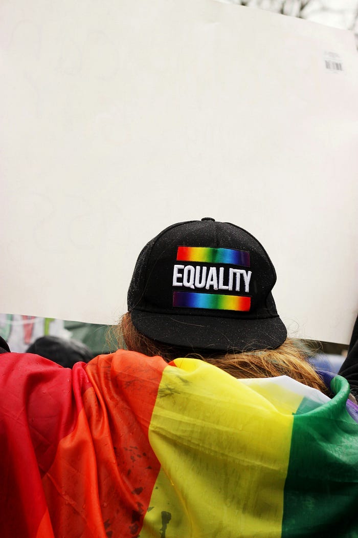 A protester wears a black baseball cap with the word ‘Equality’ printed in rainbows. Corporations often sell merchandise that appeals to the political situation in their current time. A protester wears a black baseball cap with the word ‘Equality’ printed in rainbows. Corporations often sell merchandise that appeals to the political situation in their current time.