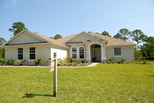 Free Beautiful suburban house with lush lawn, showcasing a for sale sign under a clear blue sky. Stock Photo