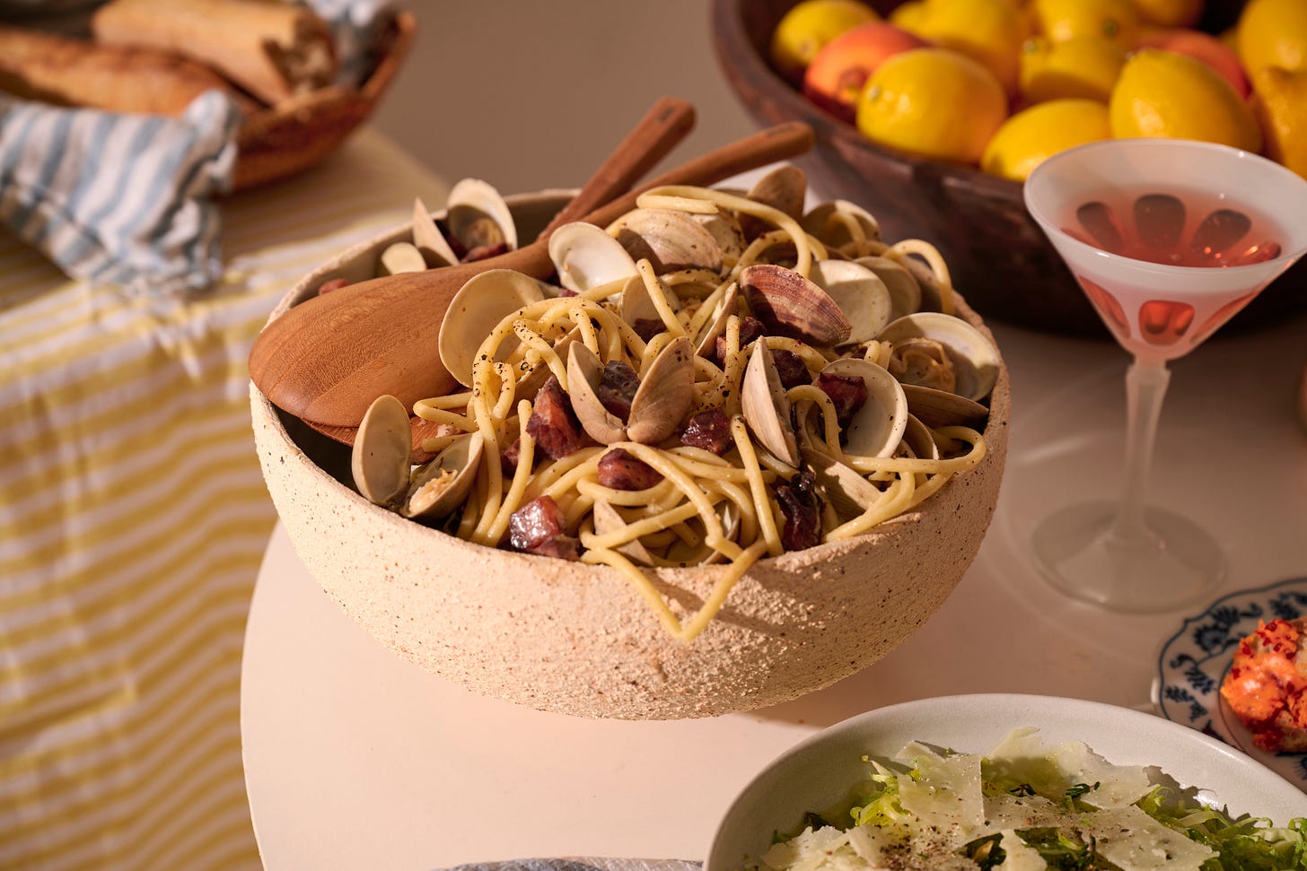 Large ceramic bowl of bucatini pasta with clams and pancetta with a wooden spoon placed over top.