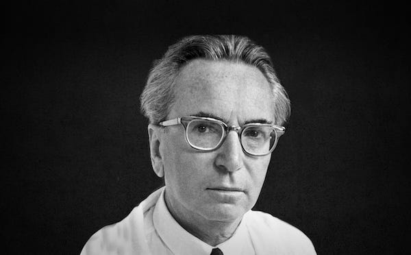 Black and white portrait of Viktor Frankl, a middle-aged man with glasses, wearing a white shirt and tie, looking directly at the camera.