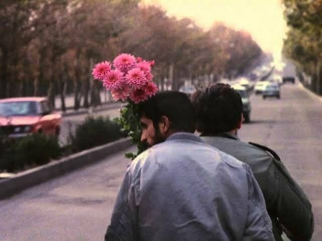 This may contain: two men are walking down the street with flowers in their hair and one is on his back This may contain: two men are walking down the street with flowers in their hair and one is on his back