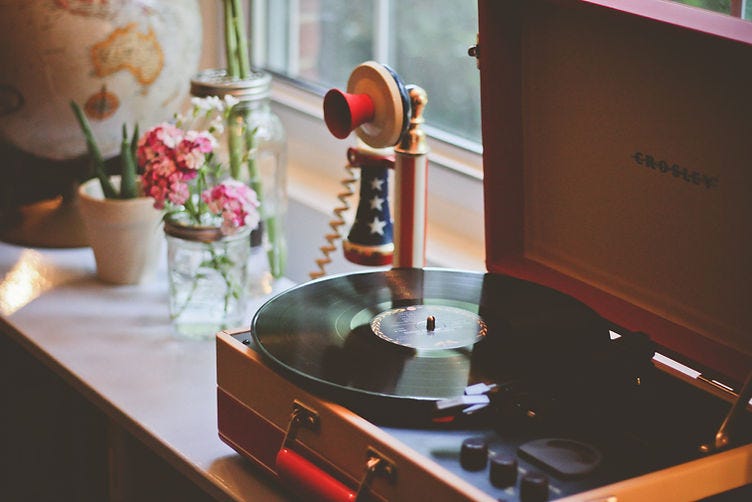 Picture of a record player sitting on a table next to a window with flowers in a vase next to it.
