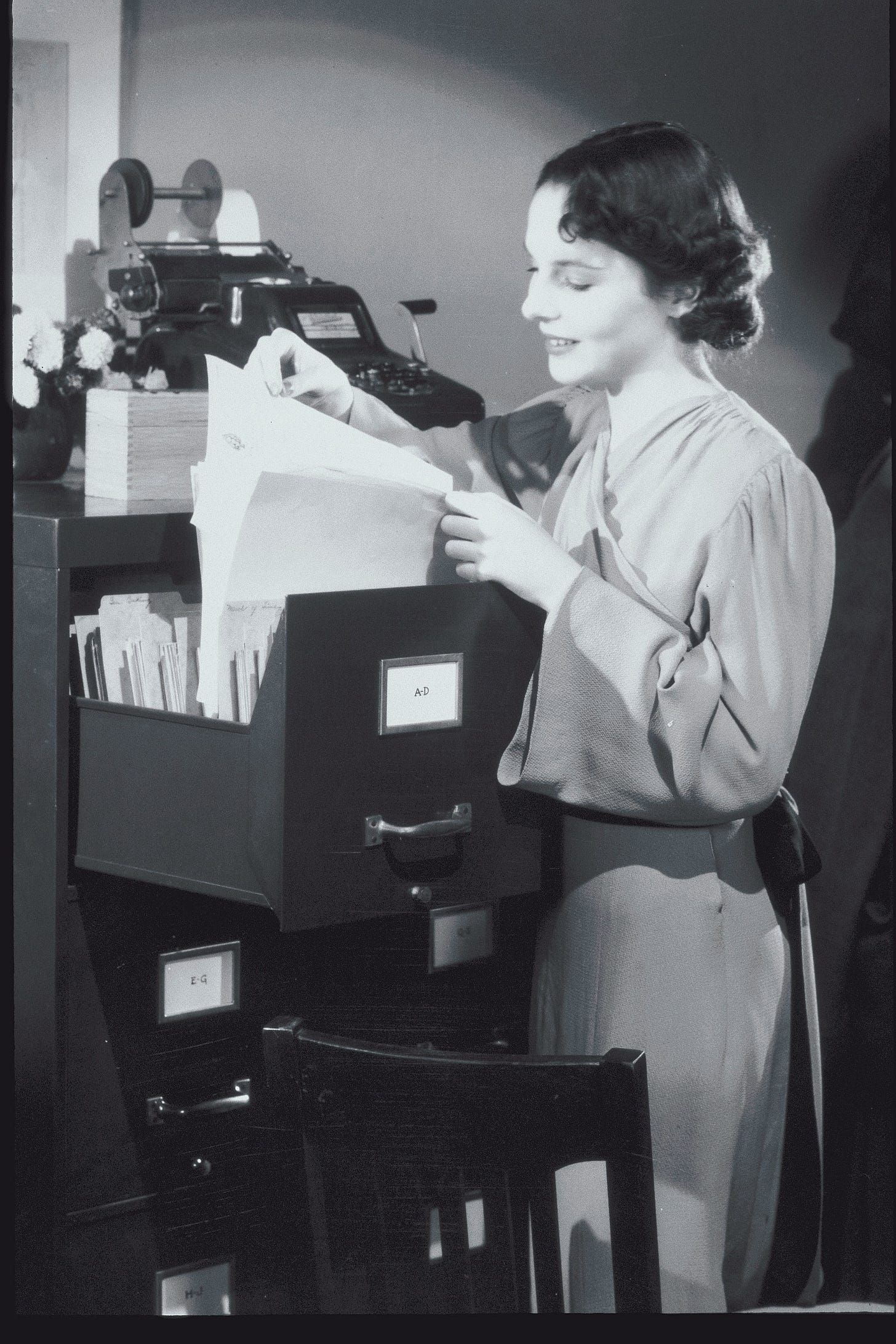 Vintage black and white photo of a woman sorting through a drawer in a filing cabinet. 