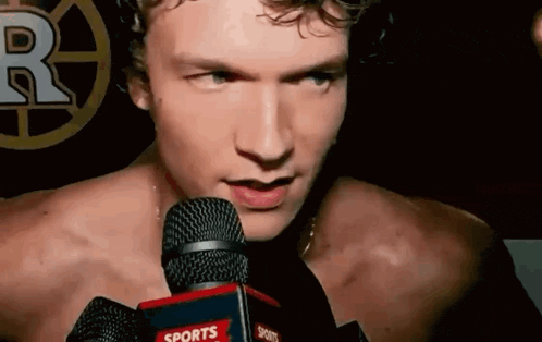 a man without a shirt is talking into a sports microphone .