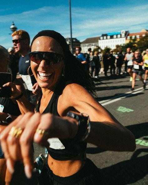 This may contain: a woman taking a selfie in the middle of a marathon with other people behind her