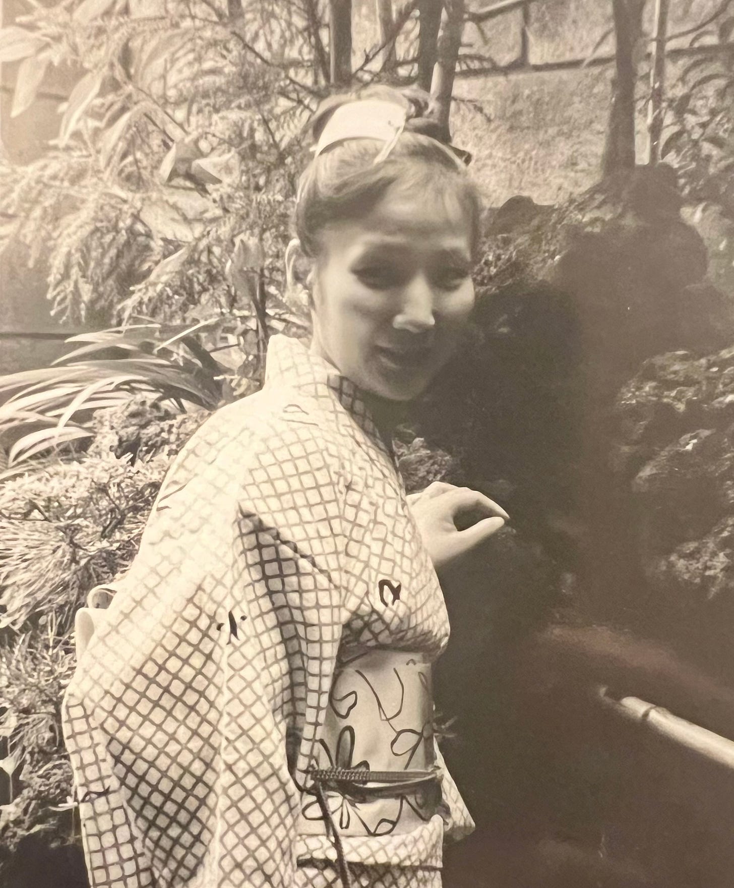 Demian's mother in Japan wearing a kimono in her uncle's garden. She's smiling at the camera. 