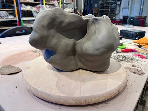 With views from different angles, 10" greenware sculpture form sitting on a wooden turn table on a clay studio table