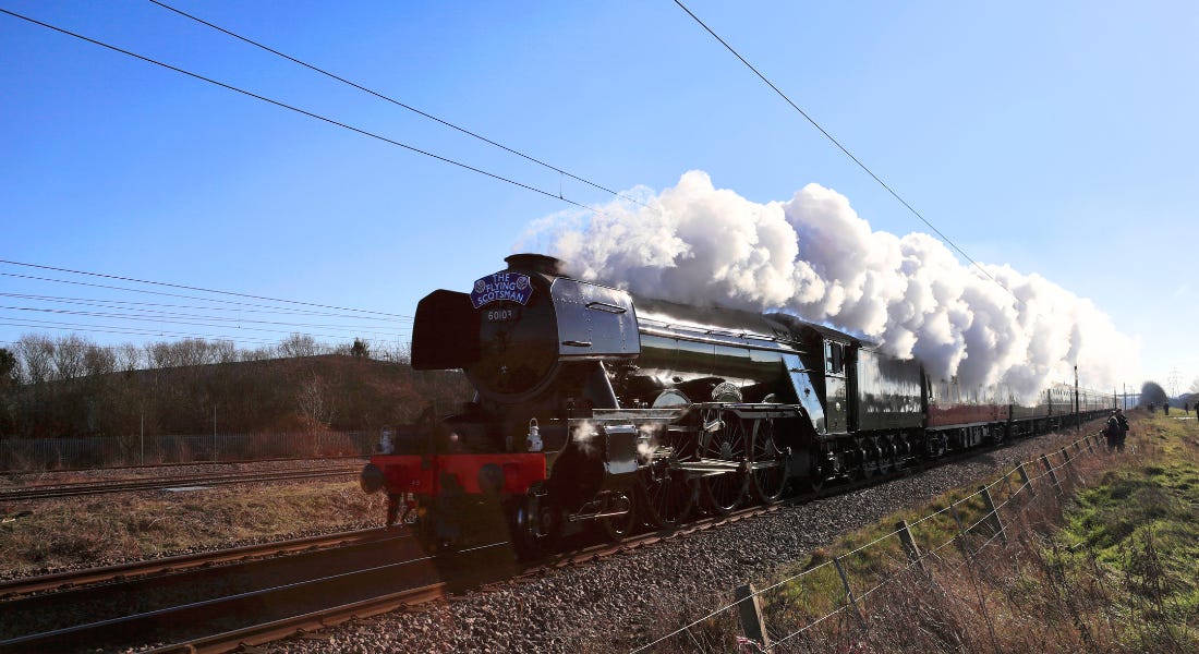 A green train - The Flying Scotsman - with steam coming out of it on a train track