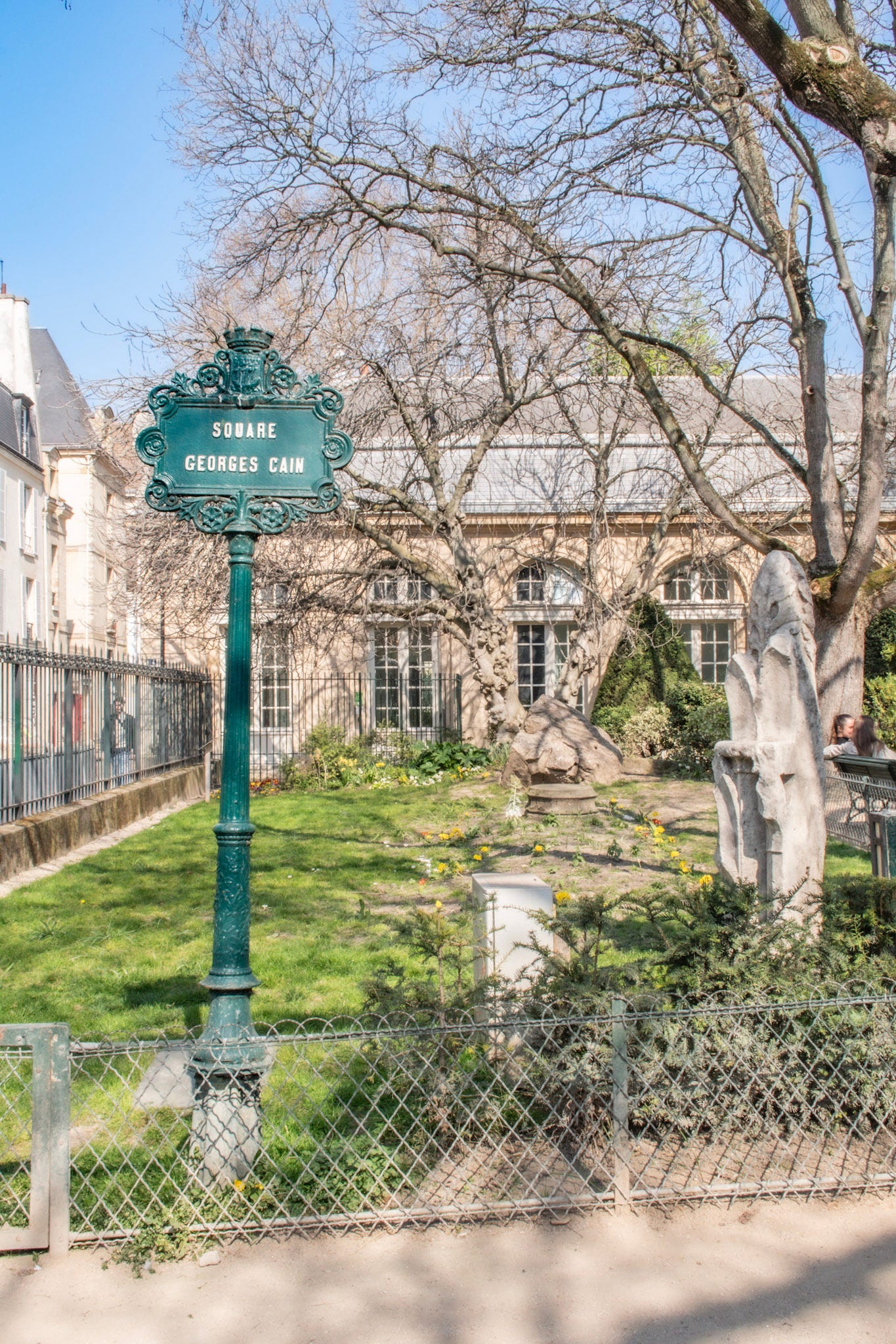Square Georges Cain sign beside historic stone fragments in the small Marais garden in Paris.
