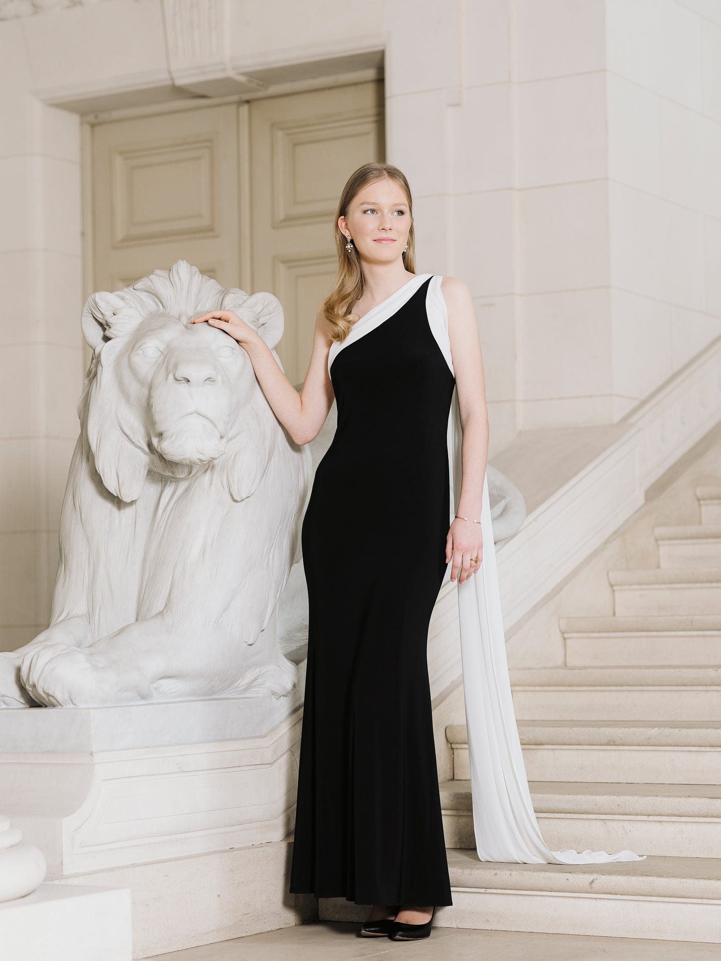Princess Éléonore of Belgium posing by a lion sculpture wearing a black and white dress