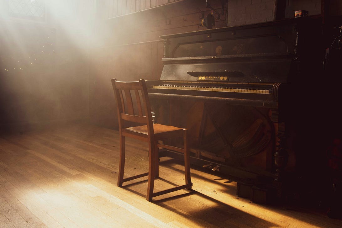Sitting chair in a dusty room facing an old piano — Photo by Paul Arky on Unsplash