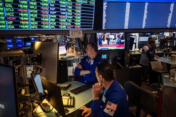 A couple of traders sit under monitors on a trading floor. 
