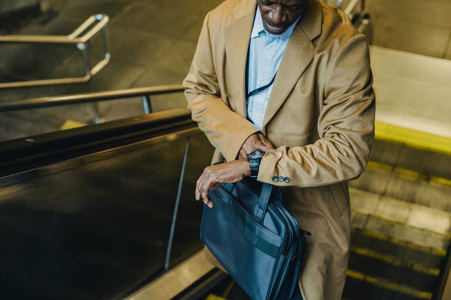 crop black businessman riding escalator and looking at wristwatch crop black businessman riding escalator and looking at wristwatch