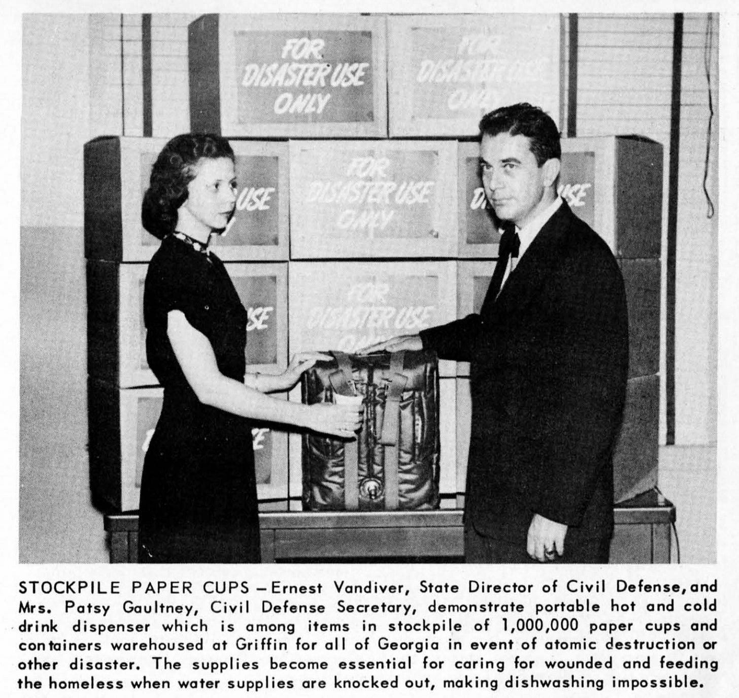 Photo from page 5 of the same issue of The Georgia Alert (November 1951), which shows a man and a woman in front of a a dozen or so boxes labeled "FOR DISASTER USE ONLY." They have their hands on something that looks like a backpack with a spigot on the front. The caption says: "STOCKPILE PAPER CUPS — Ernest Vandiver, State Director of Civil Defense, and Mrs. Patsy Gaultney, Civil Defense Secretary, demonstrate portable hot and cold drink dispenser which is among items in stockpile of 1,000,000 paper cups and containers warehoused at Griffin for all of Georgia in event of atomic destruction or other disaster. The supplies become essential for caring for wounded and feeding the homeless when water supplies are knocked out, making dishwashing impossible."