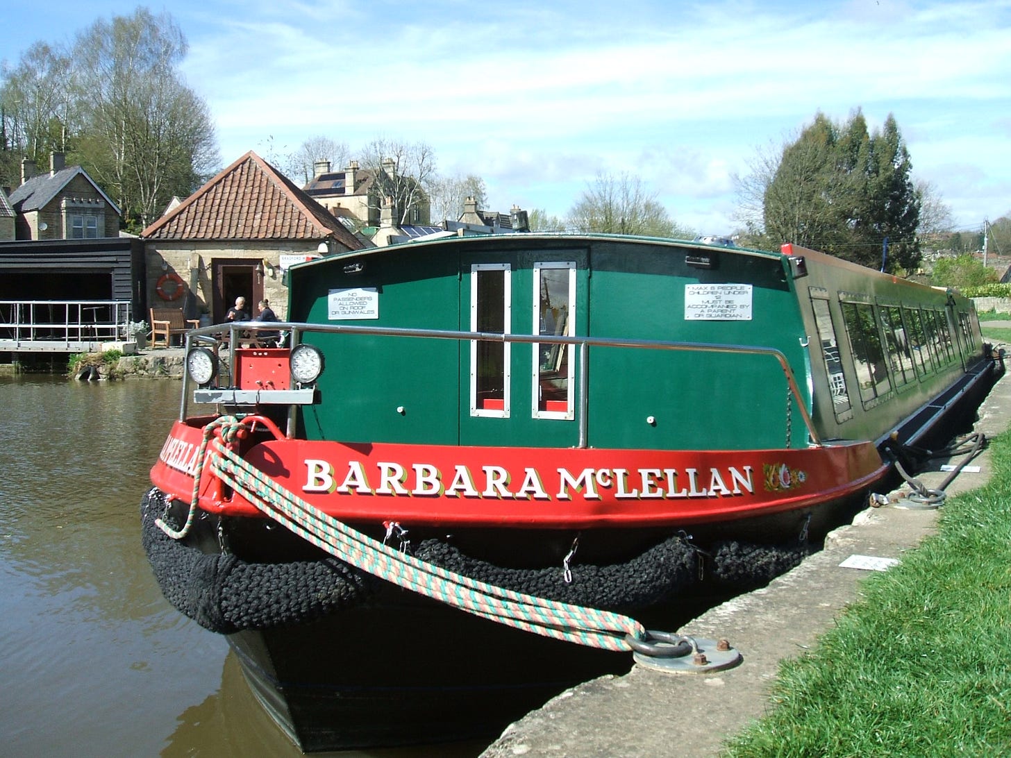 The box of a narrow boat on the Kennet and Avon Canal at Bradford on Avon, Wiltshire. The name of the boat is Barbara McCellan in white writing on a red background. The boat is predominantly green. Photo by Roland Milward