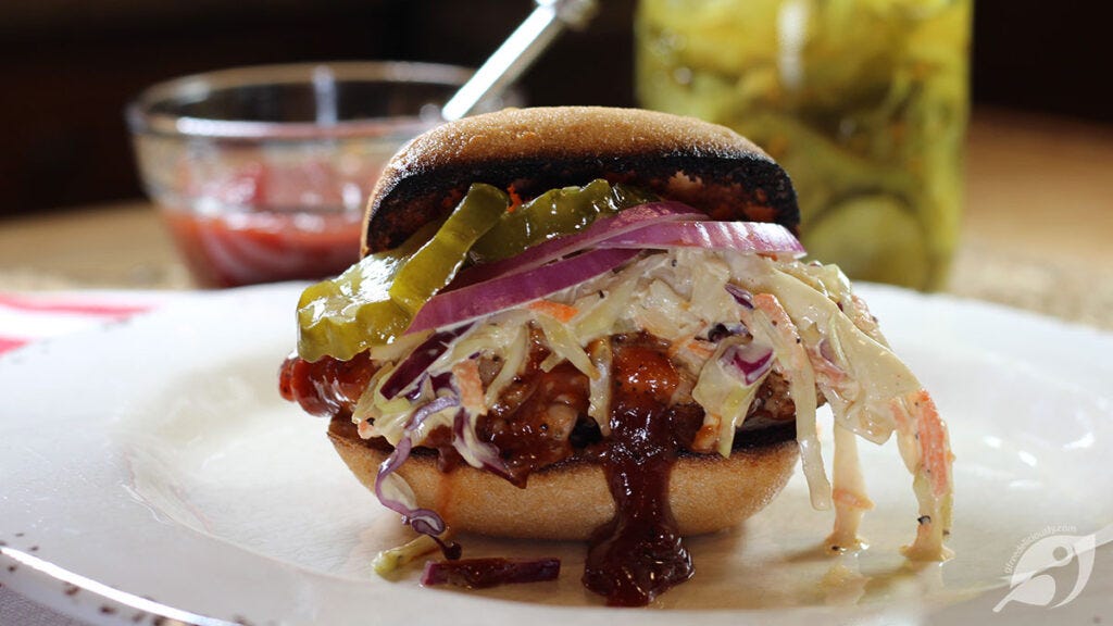 BBQ Chicken Sandwich on a plate with sauce and pickles in background BBQ Chicken Sandwich on a plate with sauce and pickles in background
