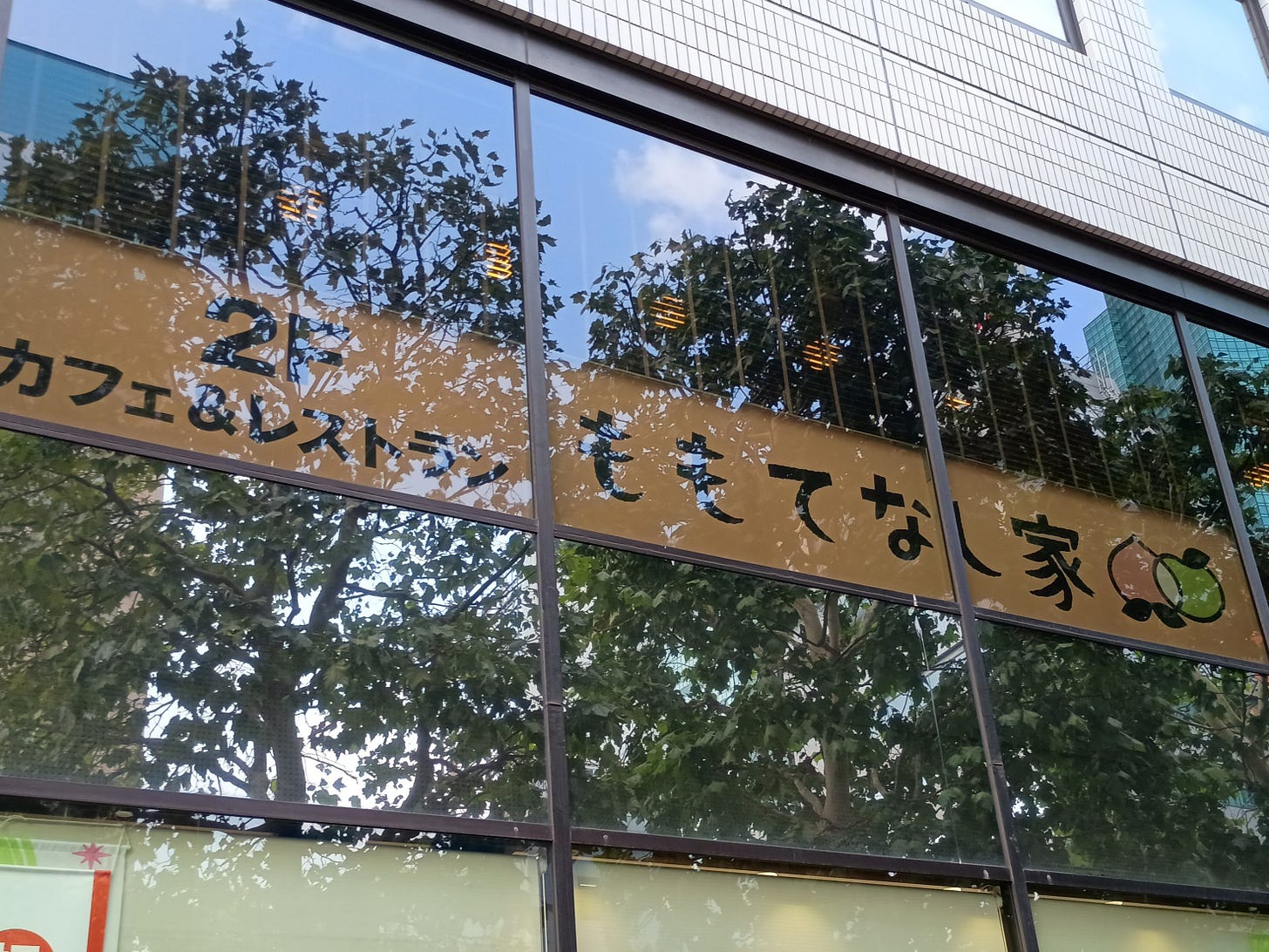新橋の岡山県・鳥取県アンテナショップの窓に掲げられた看板。「2F カフェ＆レストラン ももてなし家」の文字と、桃と梨のイラストが並ぶ