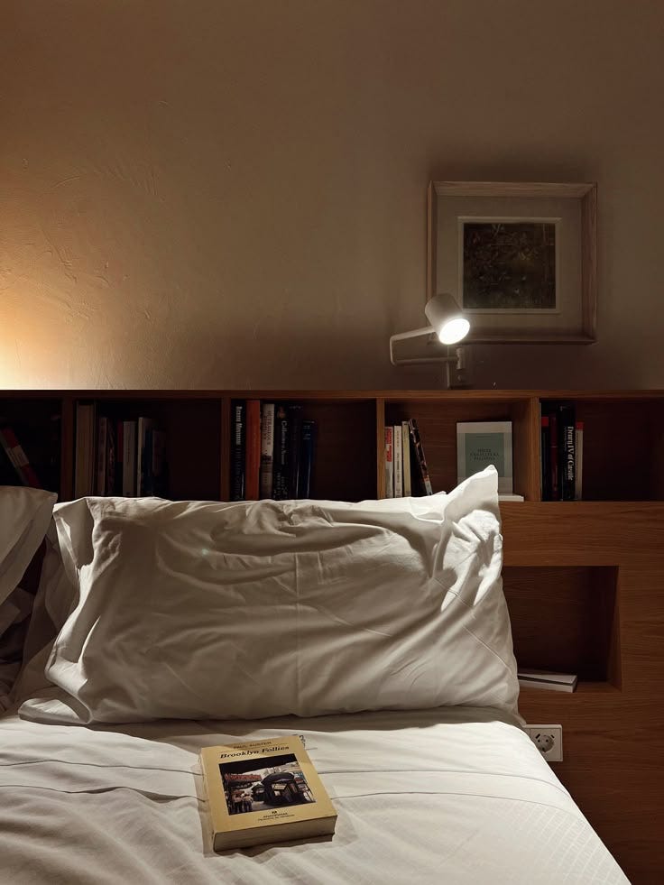 This may contain: a book is laying on top of a bed with white sheets and pillows, in front of a bookshelf