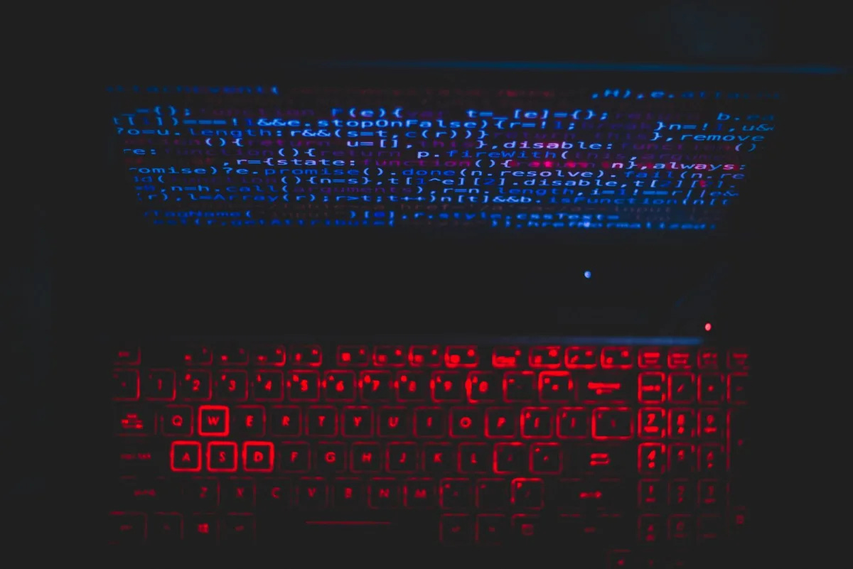 A MacBook with a code editor open, glowing blue in a dark room