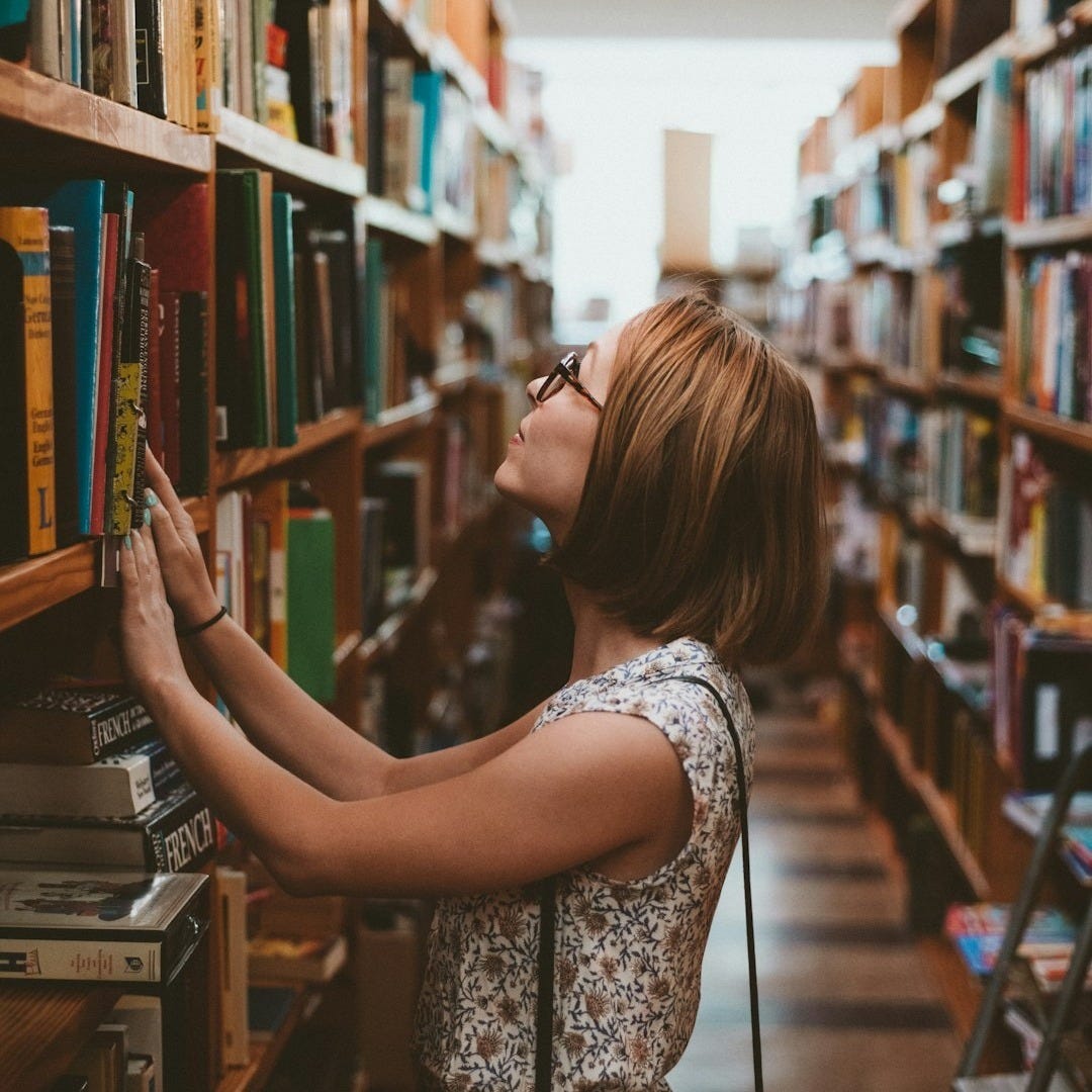 woman standing between library book shelves woman standing between library book shelves