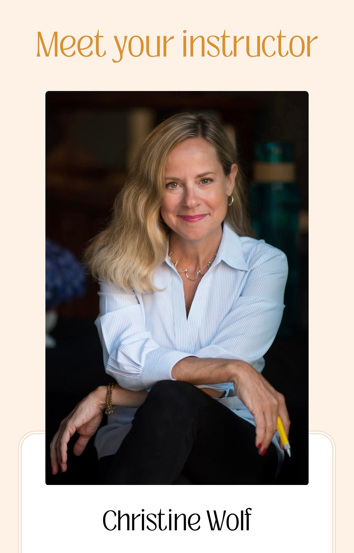 Blonde woman with shoulder-length hair in blue button-down blouse. She's smiling, her arms are crossed across her lap and she's holding a yellow pen.