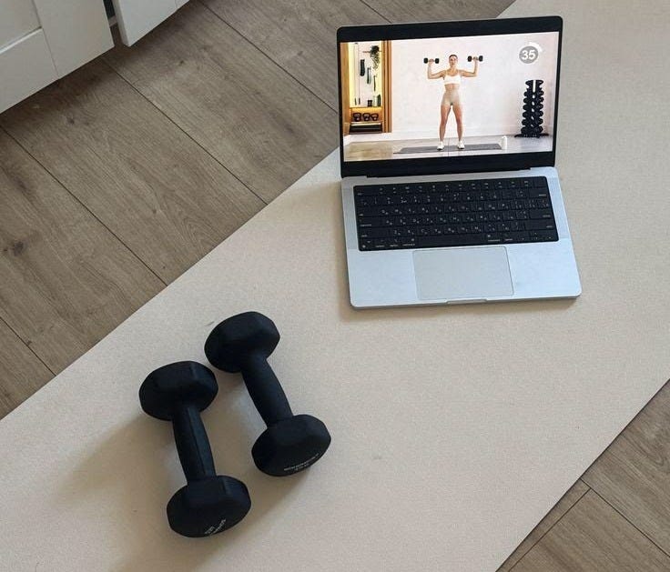 This may contain: an open laptop computer sitting on top of a wooden floor next to two black dumbs