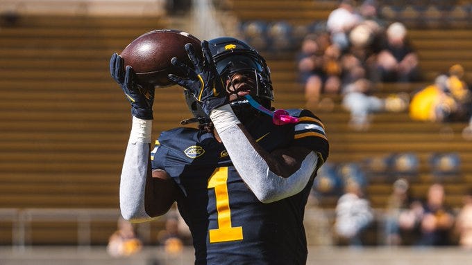 Three images of Cal Football players in navy blue and yellow uniforms on a sunny stadium field. First image shows a player with dreadlocks wearing number 20 helmet and jersey standing with teammates in the background. Second image captures a player numbered 1 catching a brown Nike football with white gloves extended. Third image depicts the same player numbered 1 holding the football overhead with one hand raised wearing a black helmet with Cal logo. Three images of Cal Football players in navy blue and yellow uniforms on a sunny stadium field. First image shows a player with dreadlocks wearing number 20 helmet and jersey standing with teammates in the background. Second image captures a player numbered 1 catching a brown Nike football with white gloves extended. Third image depicts the same player numbered 1 holding the football overhead with one hand raised wearing a black helmet with Cal logo.