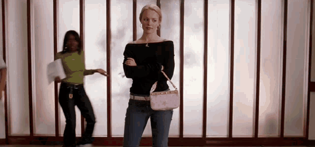 a woman standing in front of a window with her arms crossed and holding a pink purse .