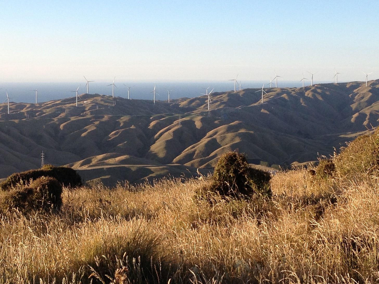 Golden hills with deep gullies, wind turbines, distant blue sea and a blue sky