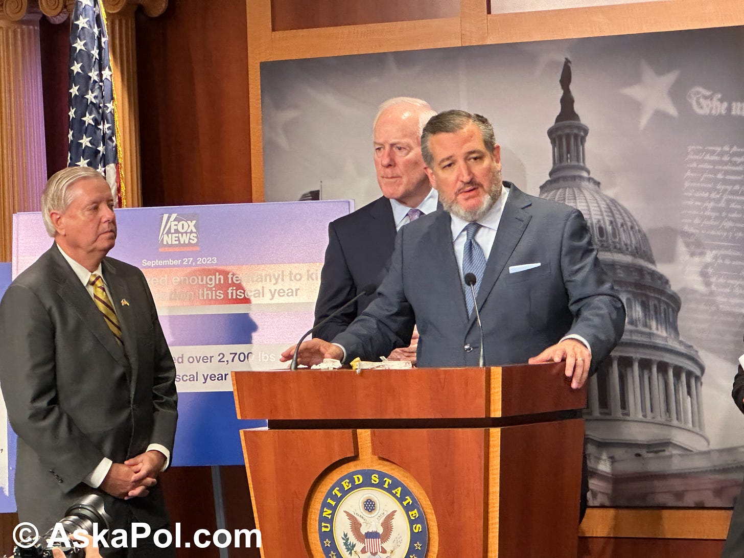 Politicians in suits and ties address a press conference from behind a podium labeled United States Senate. © www.askapolpolitics.com