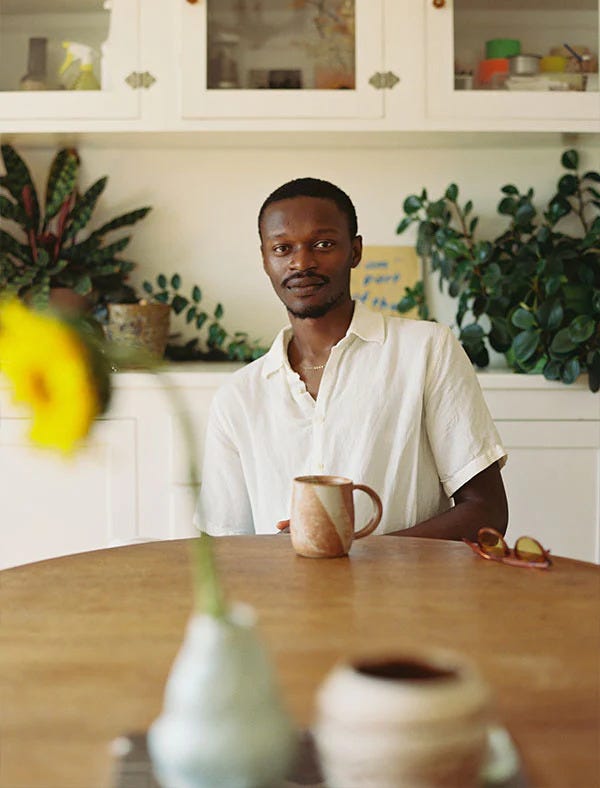 Portrait of a man with various plants and ceramics in the fore and background.