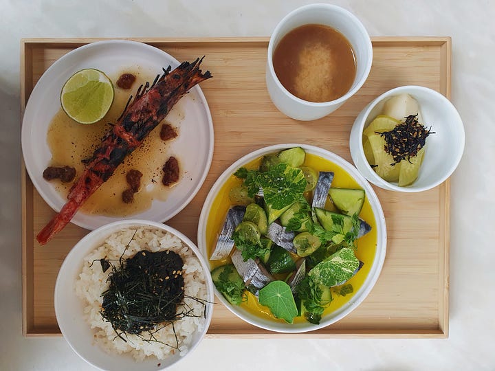 Picture one shows two crab balls topped with herbs and a glass tumbler with a drink inside. Picture two shows a tray with a dish of pickles, a dish of rice wish seaweed, a plate with a large barbecued prawn, a plate with vegetables and a cup of miso soup