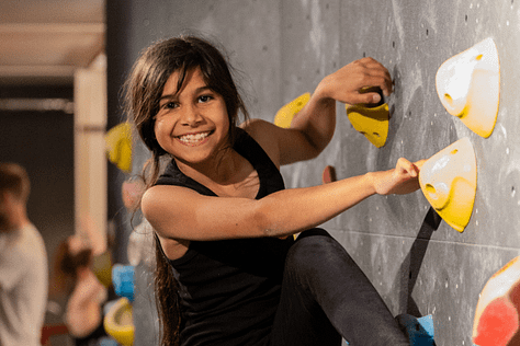 Smiling cildren of various ages climbing a climbing wall.