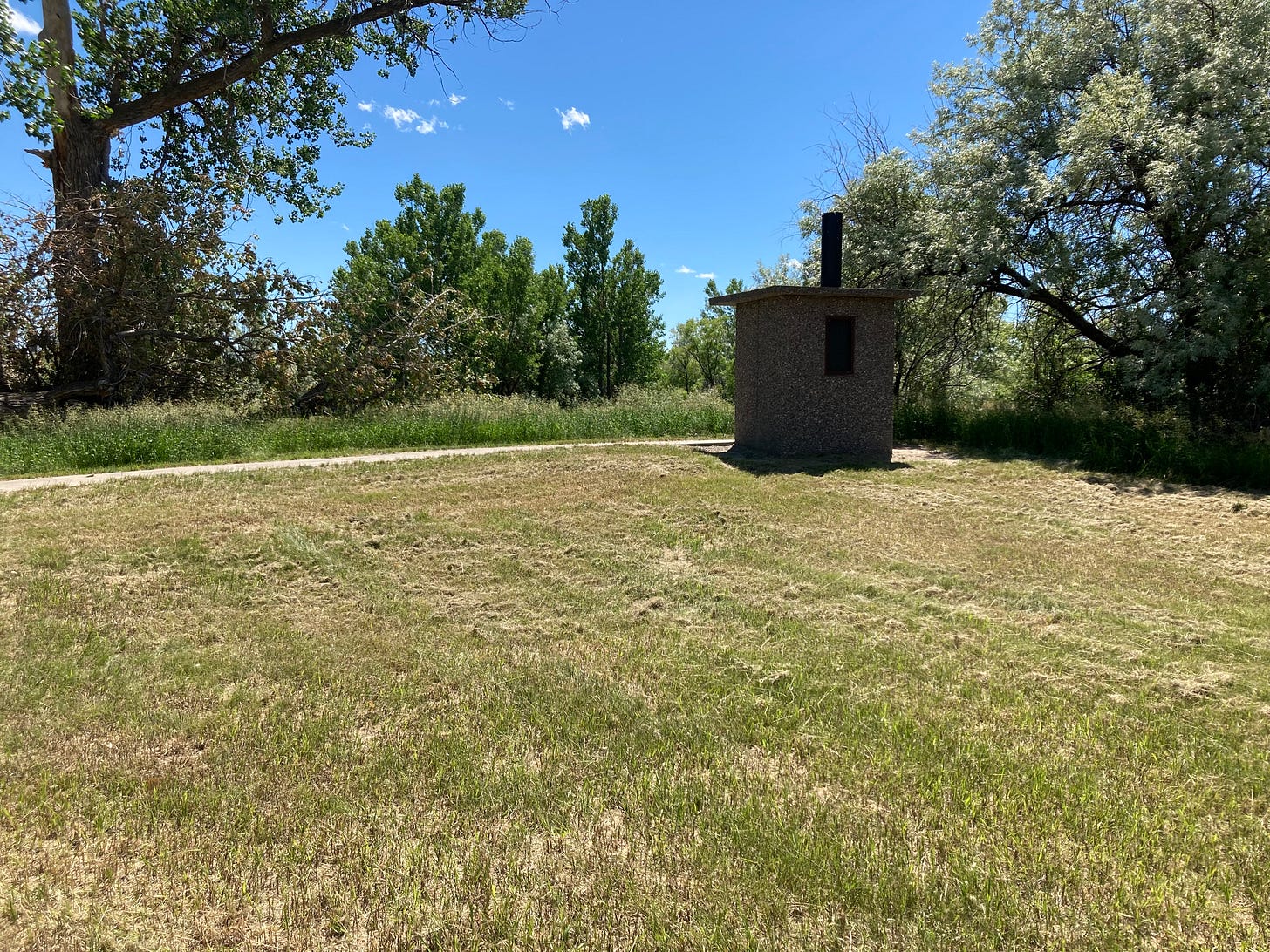 An outhouse at the end of a sidewalk in a grassy area.