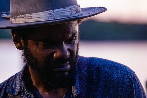 A collage of five photos of Gary Clark Jr. performing outdoors. The images are a mix of color and black and white, featuring close-ups of his face as he sings and wider shots of him playing the guitar, all while wearing his signature hat.