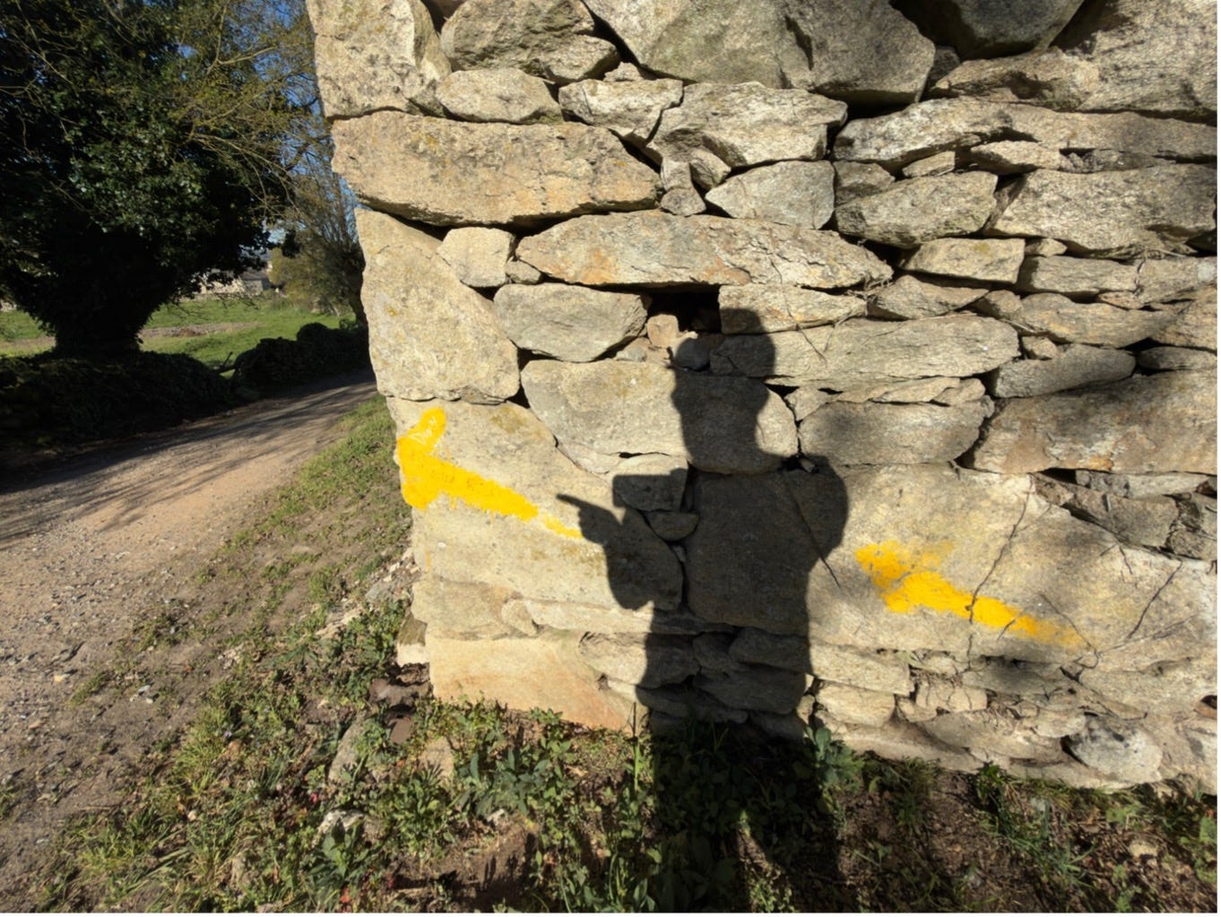 A shadow of a man pointing at a yellow arrow on a stone wall.