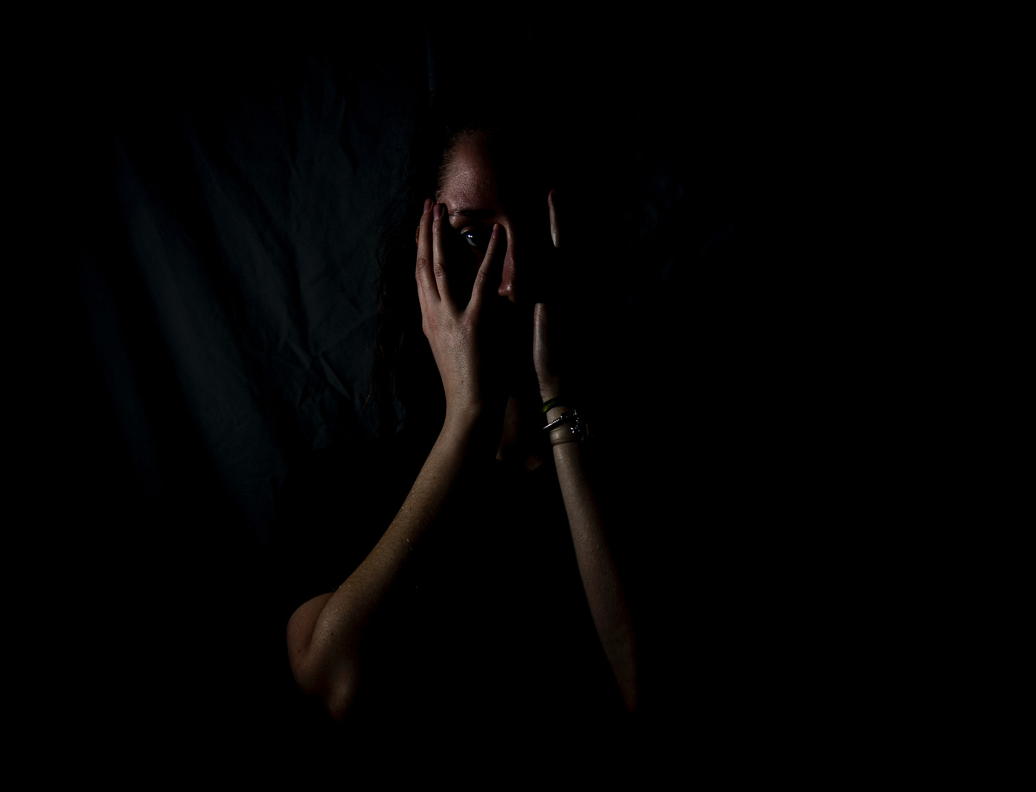 A person is holding their hands up to their face, peering through their fingers. A person is holding their hands up to their face, peering through their fingers.