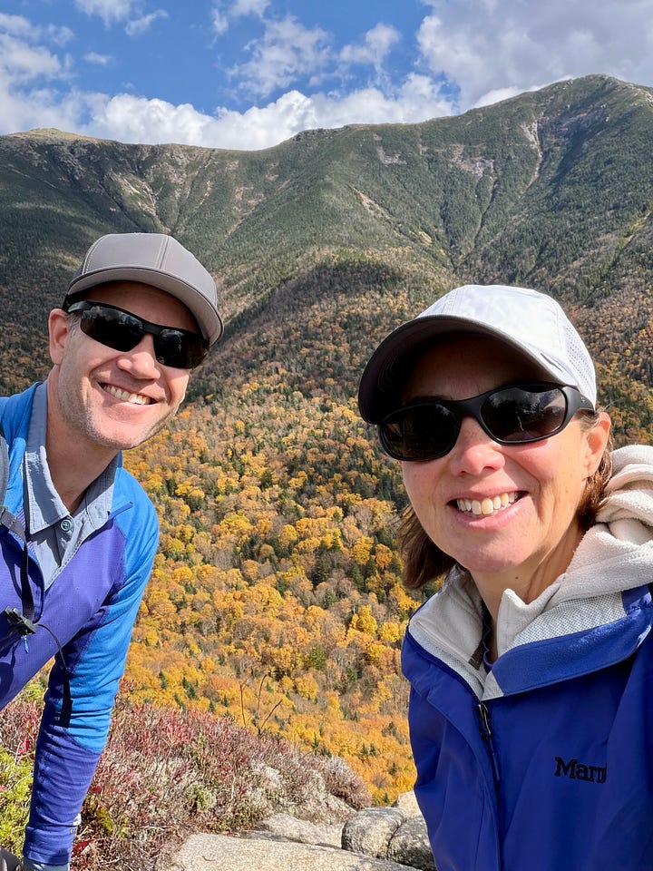 two hikers at an overlook of Franconia Ridge and path through the trees with leaves covering the trail