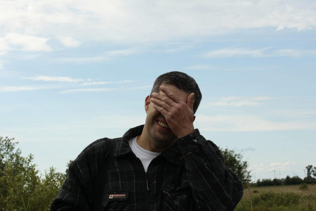 Blue sky with clouds and a man standing in front with a black zip up jacket and his hand over his eyes in frustration Blue sky with clouds and a man standing in front with a black zip up jacket and his hand over his eyes in frustration