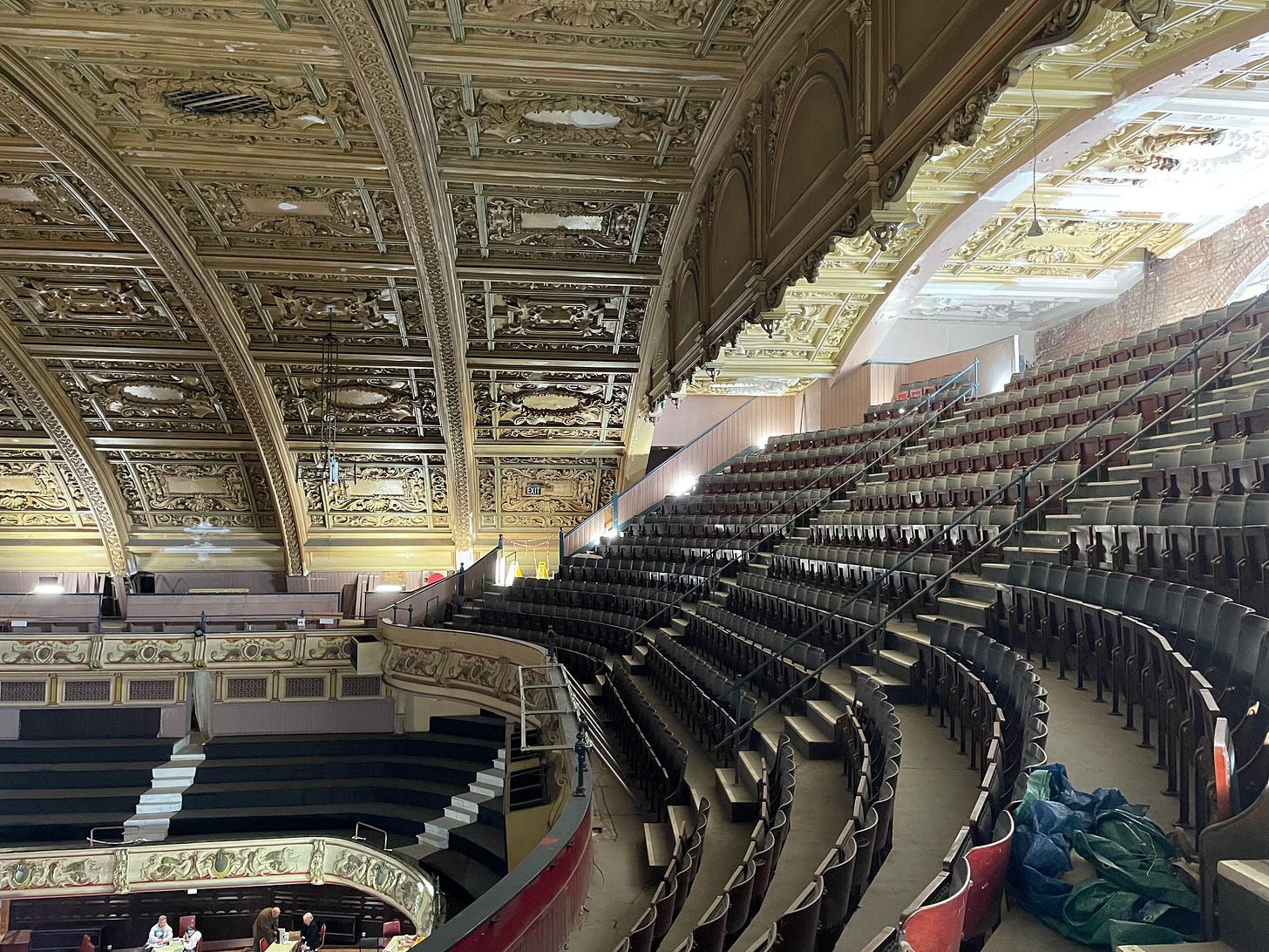 The interior of the Winter Garden. In the upper circle, rows of old wooden seats are still in place, and the elaborate plaster ceiling curves up above them. The theatre is clearly still being renovated, but you can't hide it's inherent grandeur even under layers of dust.