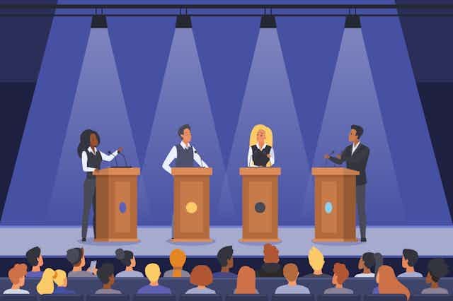 Two women and two men at lecterns on a stage above an audience. Two women and two men at lecterns on a stage above an audience.
