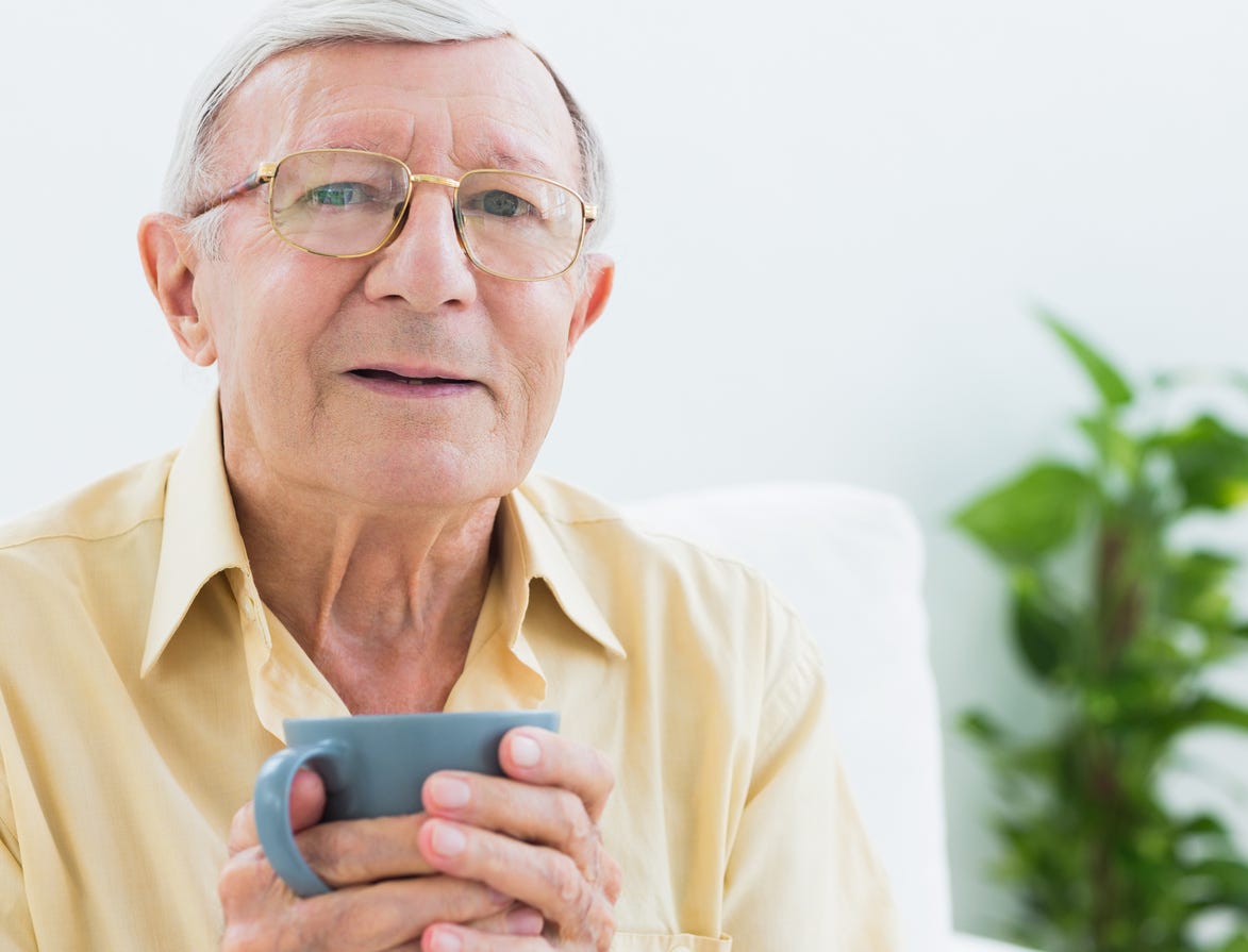 White man with gray hair and glasses holding coffee cup with both hands.