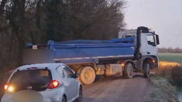 Reversing Blue open back lorry covered in tarpaulin, No number plates. Early morning with lights on.