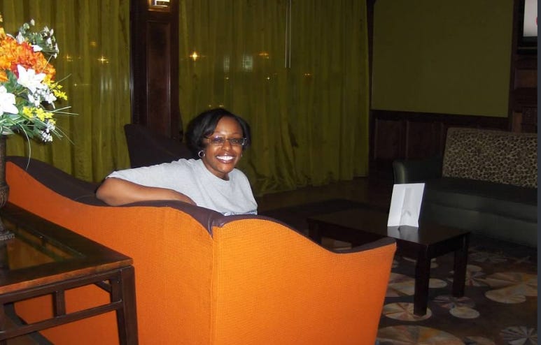 Black woman in glasses sits in green and orange hotel lobby