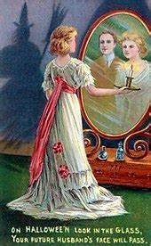 Illustrazione vintage di una ragazza bionda in abiti vittoriani, con in mano una candela, che sta davanti a uno specchio. Oltre al suo riflesso, appare il volto di un uomo. Sulla parete accanto a lei c'è l'ombra di una strega con cappello a punta. Sotto all'immagine è scritto "on halloween look in the glass, your husband's face will pass"