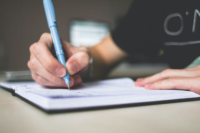 Person holding a pen while writing in a paper journal. Person holding a pen while writing in a paper journal.