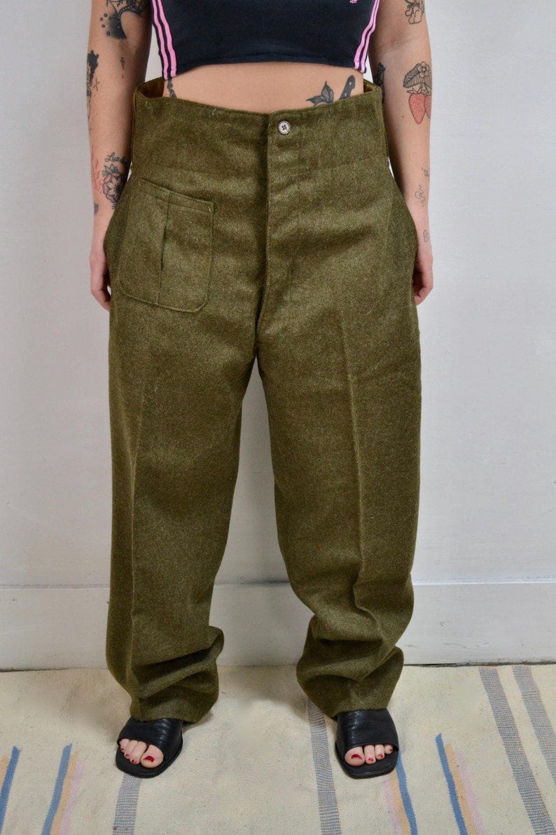 May include: High waisted green wool pants with a large pocket on the left side.
