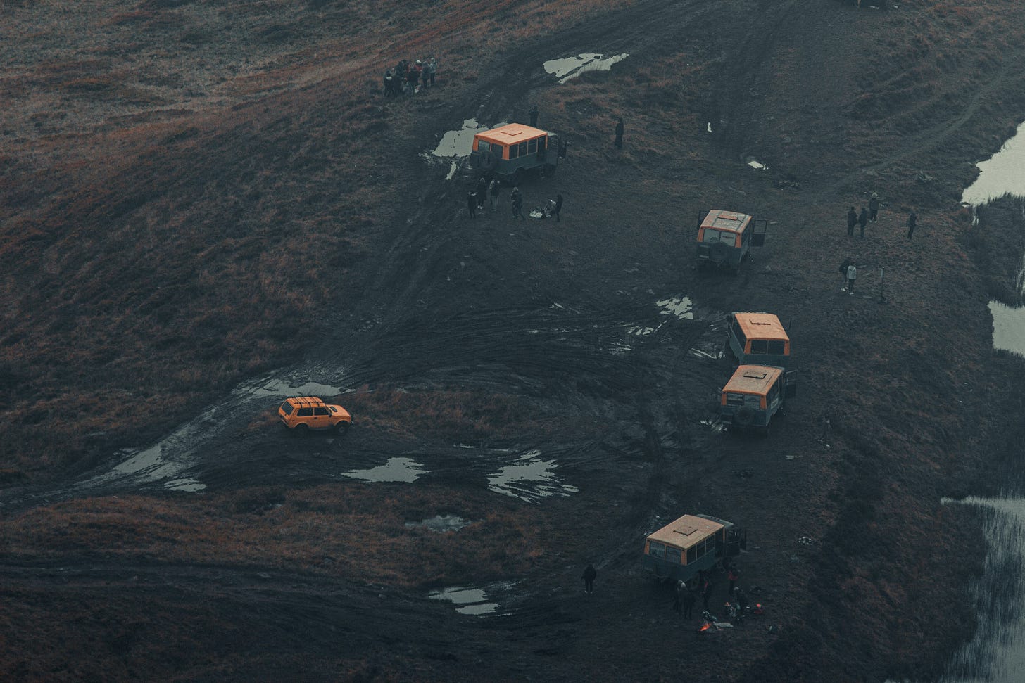 A photograph of a field of dirt with cars and people on it.