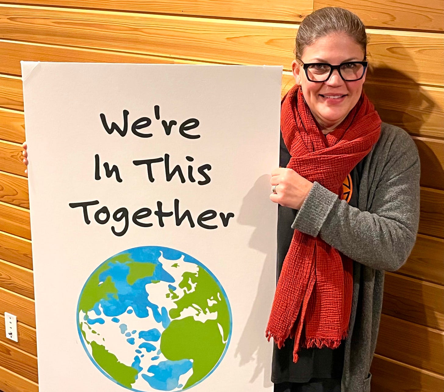 Tracy holding a rally sign that has a picture of a globe and the words "we're in this together"